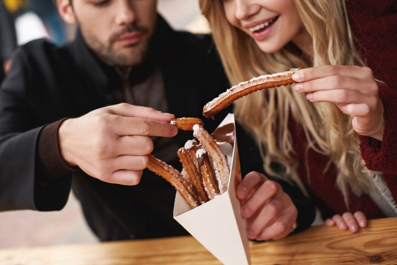 Close-up of young couple are eating churros at the street food market