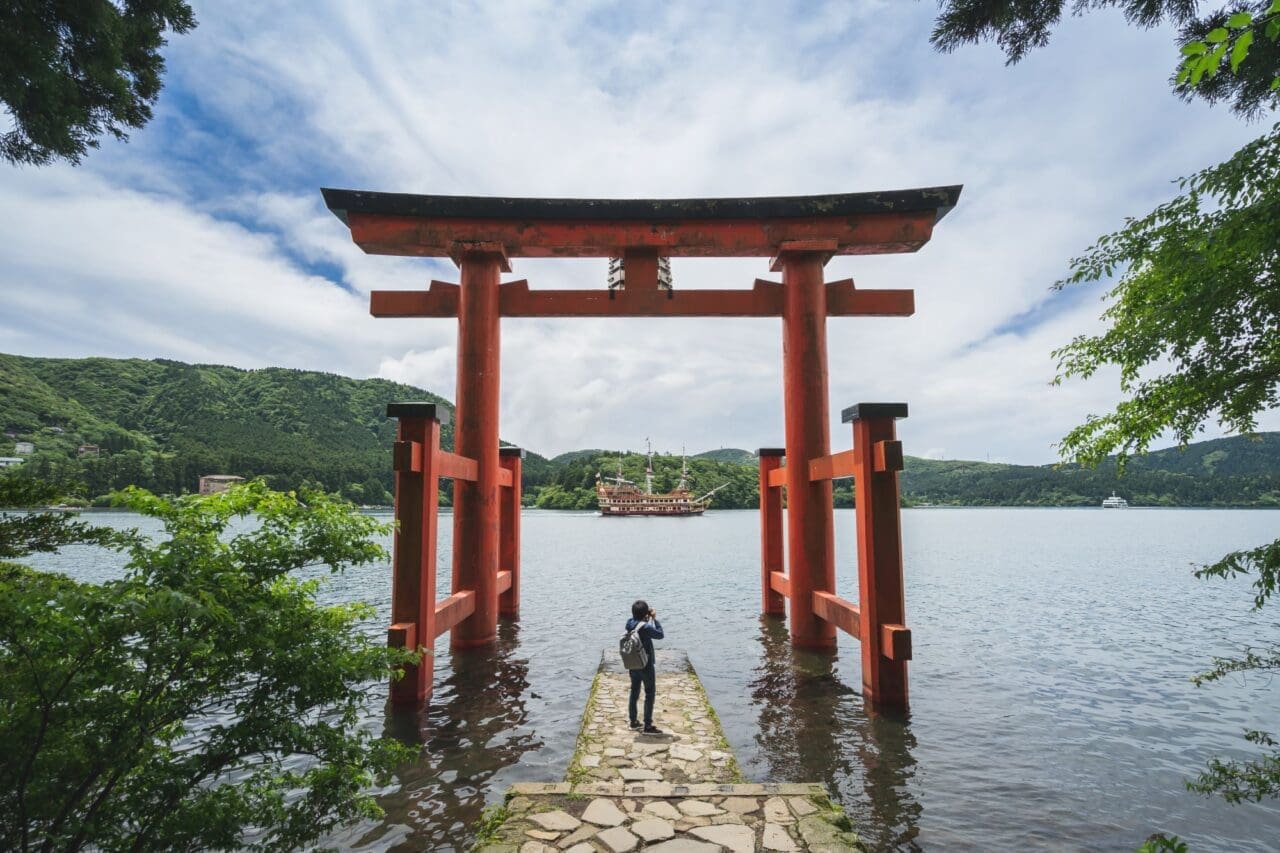 Young traveler taking photo at red Torii gate of Hakone shrine at lake Ashi, Japan