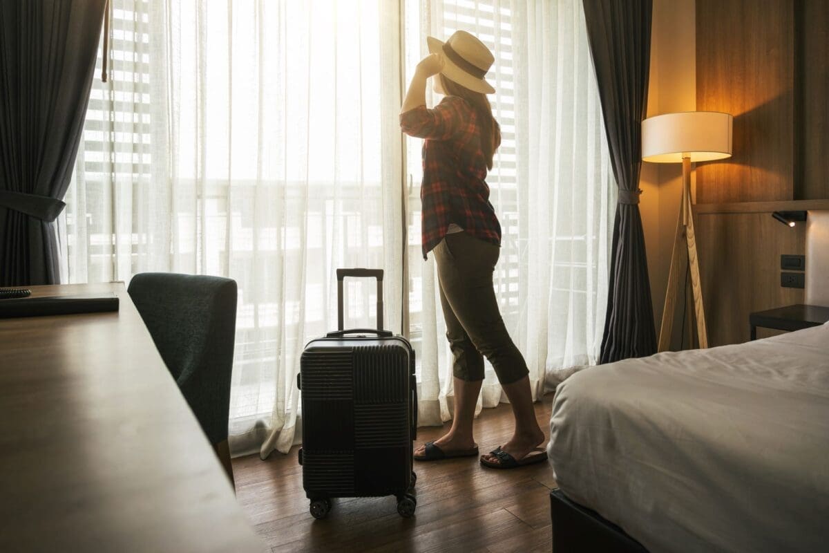 Asian traveler woman standing with baggage in bedroom of hotel or hostel-how to find affordable accommodation and transportation when traveling