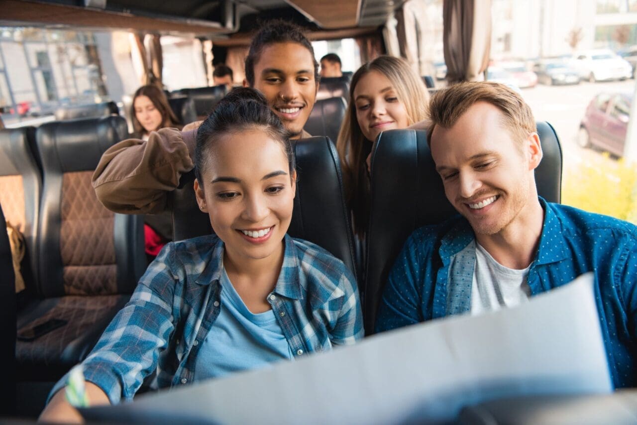 cheerful multiethnic tourists looking at map during trip on travel bus
